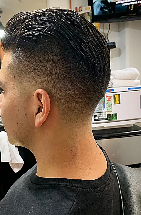 Degradado alto en la nuca con el cabello largo peinado hacia atrás.