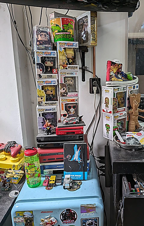 Repisa con figuras Funko Pop, Tortugas Ninja y piezas de Star Wars junto a la estación de trabajo.