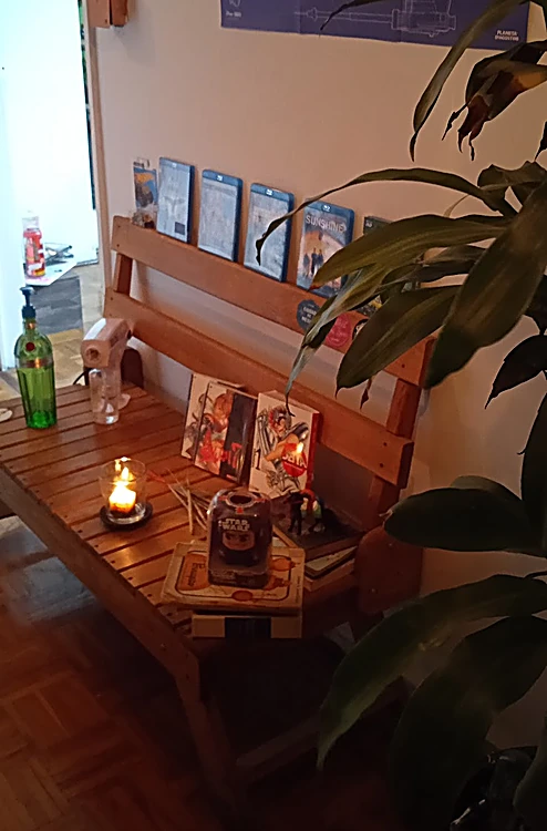 Sala de espera: banca de madera con una vela encendida, plantas y películas en la repisa.